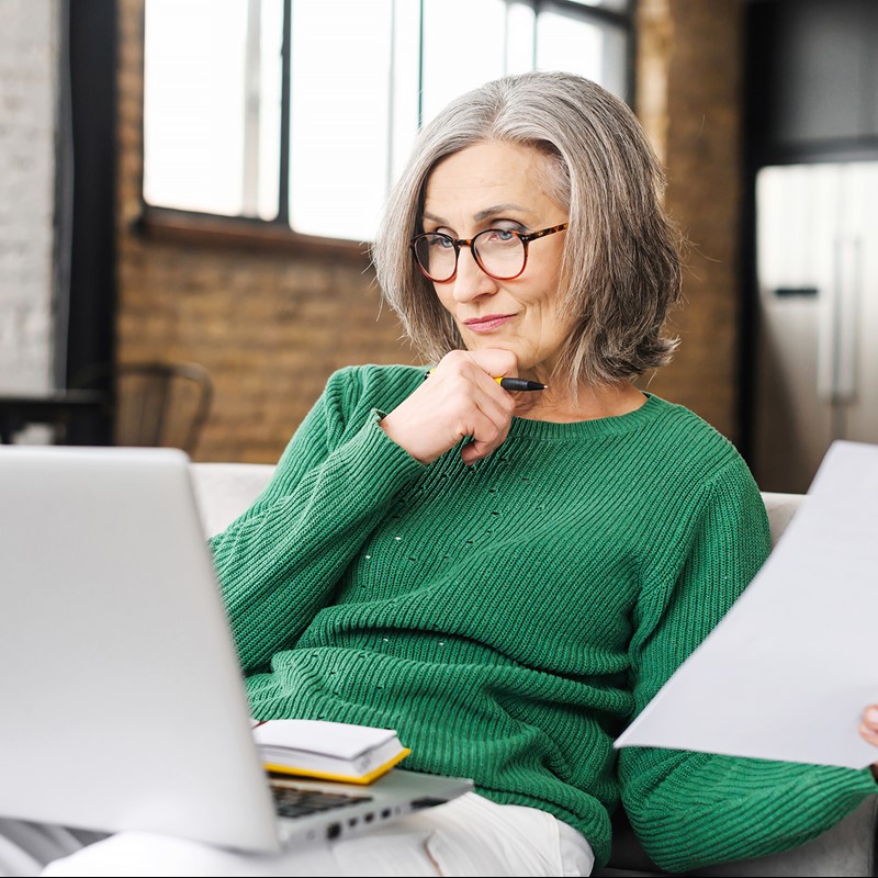 Woman wearing a green jumper looks inquisitively at a laptop